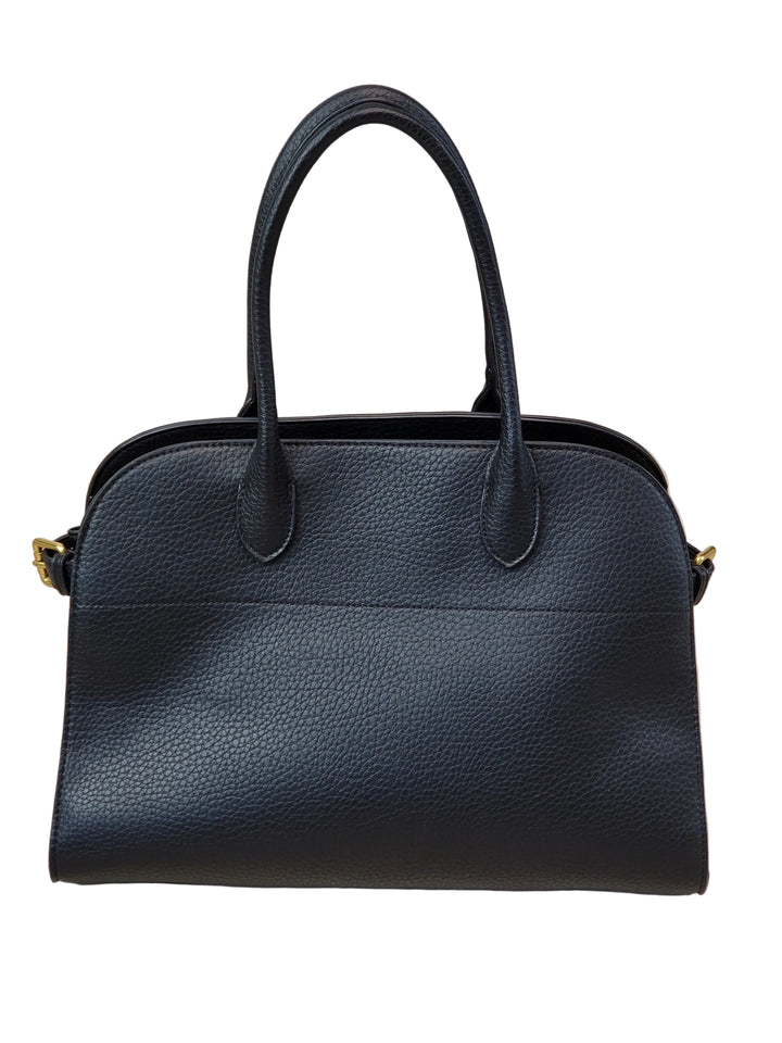 Black leather handbag on a light wooden floor with a white wall background