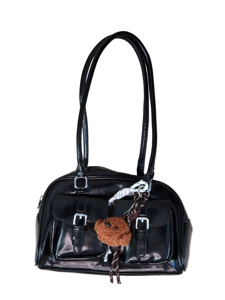 Black handbag with decorative keychain on a light wooden floor